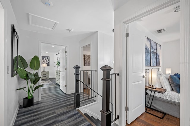 corridor featuring dark wood finished floors, visible vents, attic access, an upstairs landing, and baseboards