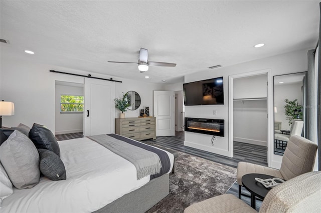 bedroom with a barn door, visible vents, a glass covered fireplace, wood finished floors, and a textured ceiling