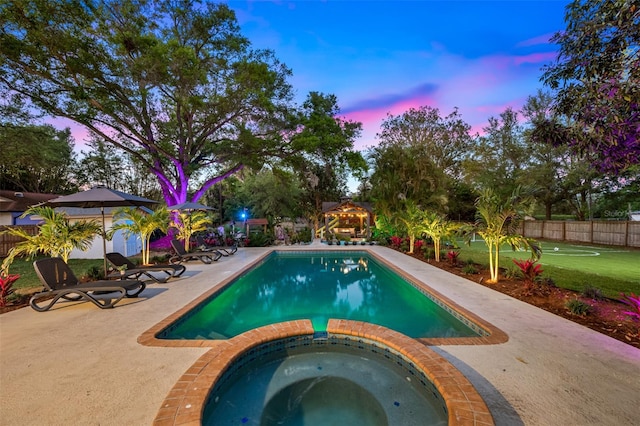 pool at dusk featuring a patio area, a pool with connected hot tub, and fence