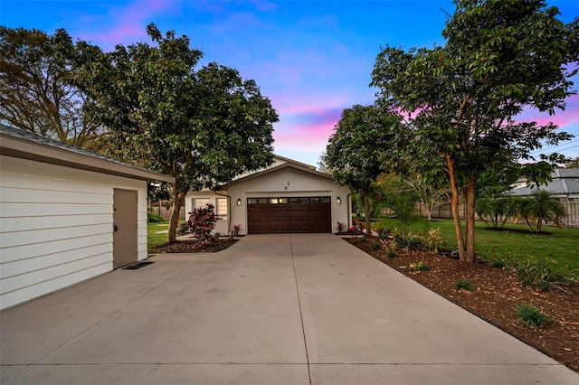 garage at dusk featuring concrete driveway and a lawn