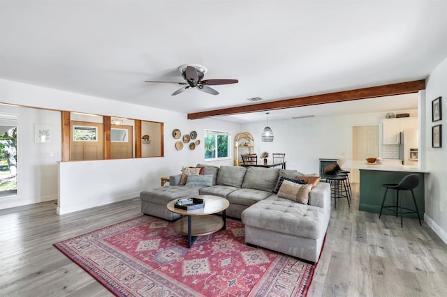 living area featuring ceiling fan, visible vents, baseboards, light wood-style floors, and beam ceiling