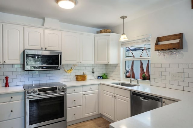 kitchen with white cabinets, appliances with stainless steel finishes, light countertops, pendant lighting, and a sink