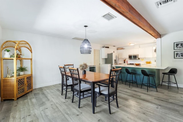 dining room with light wood finished floors, beam ceiling, and visible vents