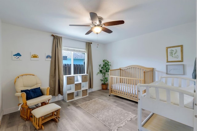 bedroom featuring a nursery area, baseboards, and wood finished floors