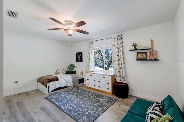 bedroom with a ceiling fan, visible vents, baseboards, and wood finished floors