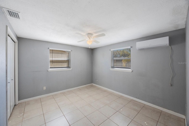 tiled empty room featuring a healthy amount of sunlight, visible vents, ceiling fan, and a wall mounted AC