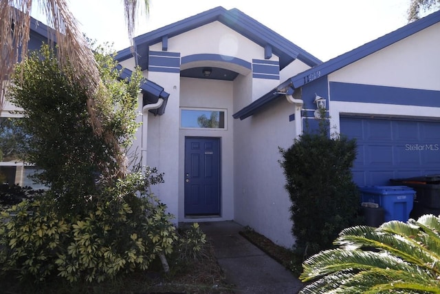 entrance to property featuring an attached garage and stucco siding