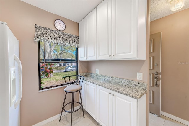 kitchen with light tile patterned floors, baseboards, white cabinets, light stone counters, and white fridge with ice dispenser