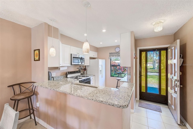 kitchen featuring light stone counters, a peninsula, white appliances, white cabinetry, and decorative light fixtures