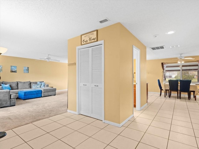 hall with visible vents, light colored carpet, a textured ceiling, and light tile patterned flooring