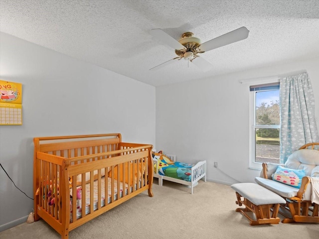 carpeted bedroom with a nursery area, a textured ceiling, a ceiling fan, and baseboards