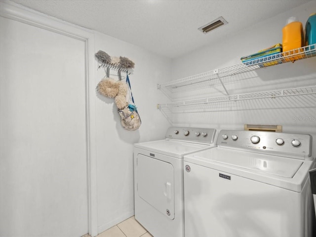 laundry area featuring light tile patterned floors, a textured ceiling, laundry area, visible vents, and washing machine and clothes dryer