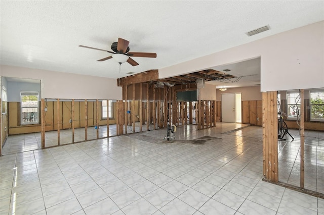 tiled spare room featuring a textured ceiling, ceiling fan, a wealth of natural light, and visible vents