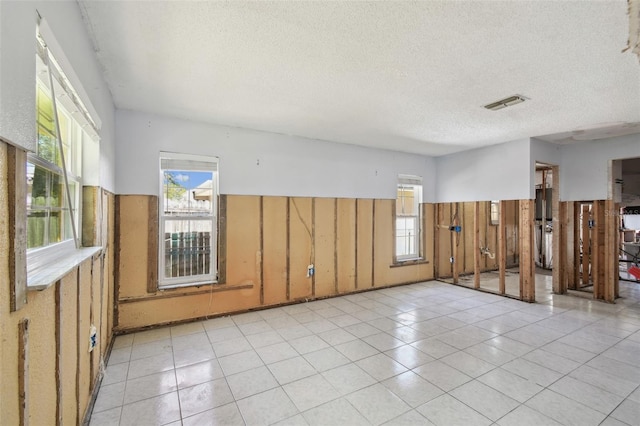 empty room featuring a textured ceiling, a wainscoted wall, visible vents, and a healthy amount of sunlight