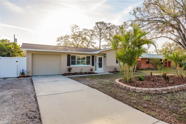 ranch-style house with a garage, concrete driveway, stucco siding, fence, and a gate