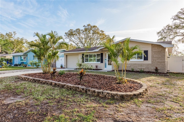 ranch-style house with an attached garage, driveway, stone siding, and fence