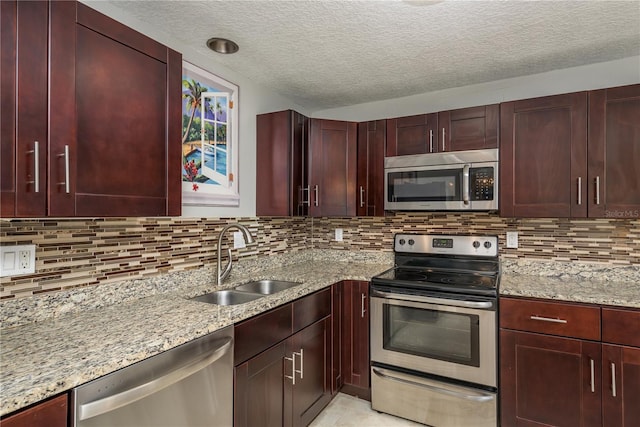 kitchen with stainless steel appliances, a sink, dark brown cabinets, light stone counters, and a textured ceiling