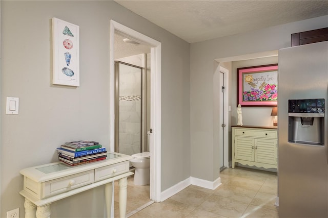 hallway featuring light tile patterned floors, baseboards, and a textured ceiling