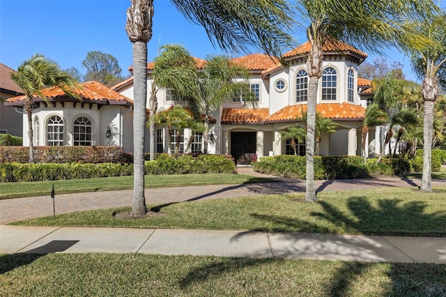 mediterranean / spanish-style house with stucco siding, a tiled roof, and a front lawn