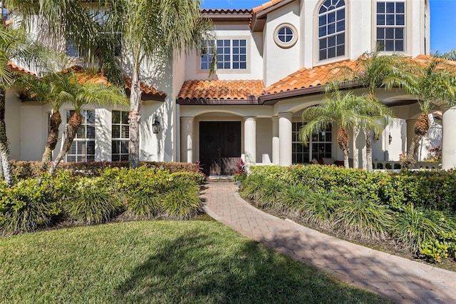 mediterranean / spanish home featuring stucco siding, a front lawn, and a tiled roof