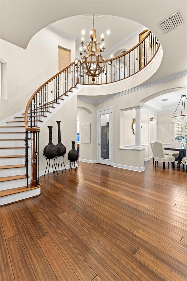 entrance foyer featuring wood finished floors, visible vents, arched walkways, crown molding, and a chandelier