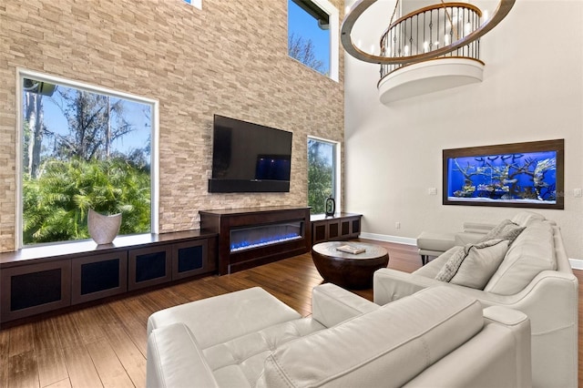 living area featuring a glass covered fireplace, baseboards, wood finished floors, and a towering ceiling