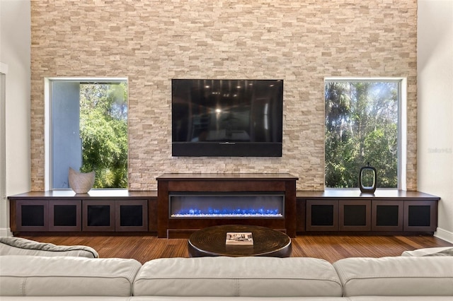 living area featuring plenty of natural light, a glass covered fireplace, and wood finished floors