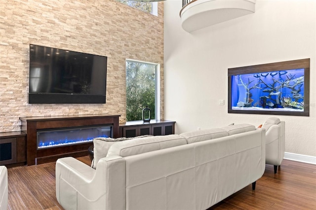 living room featuring a glass covered fireplace, wood finished floors, baseboards, and a towering ceiling