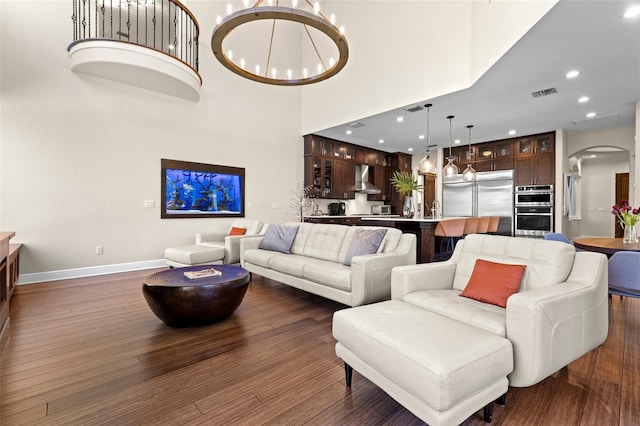 living area featuring visible vents, a high ceiling, an inviting chandelier, arched walkways, and dark wood-style flooring