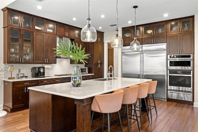 kitchen with light countertops, wood finished floors, stainless steel appliances, a warming drawer, and a sink