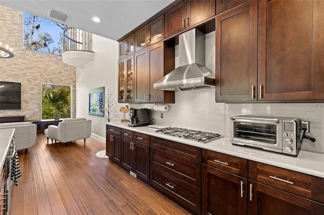 kitchen featuring stainless steel gas cooktop, open floor plan, light countertops, and wall chimney range hood