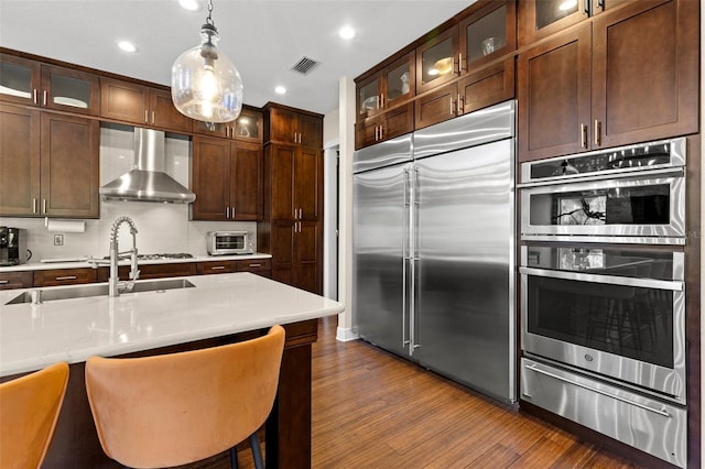 kitchen with a warming drawer, visible vents, dark wood finished floors, stainless steel appliances, and wall chimney range hood