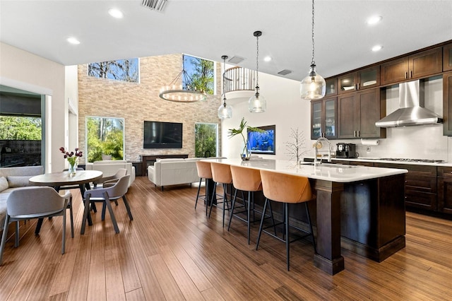 kitchen featuring a center island with sink, a sink, open floor plan, wall chimney exhaust hood, and light countertops