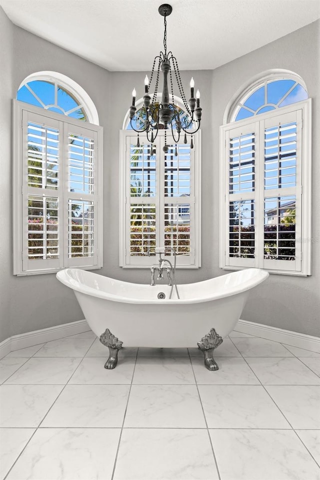 full bath with a soaking tub, marble finish floor, an inviting chandelier, and baseboards