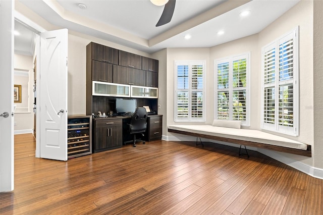 home office with a raised ceiling, wood finished floors, built in desk, wine cooler, and baseboards