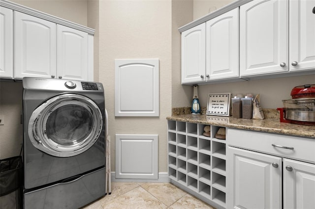 washroom featuring light tile patterned floors, baseboards, washer / clothes dryer, and cabinet space