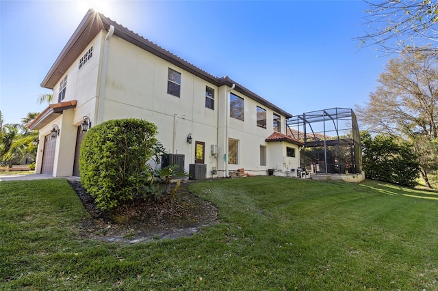 rear view of house with a tile roof, central AC, glass enclosure, a yard, and an attached garage