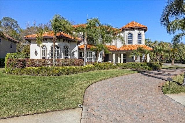 mediterranean / spanish-style house featuring stucco siding, a tile roof, decorative driveway, and a front lawn