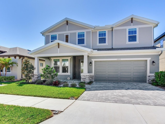 view of front of house featuring a garage, stone siding, a front lawn, and decorative driveway