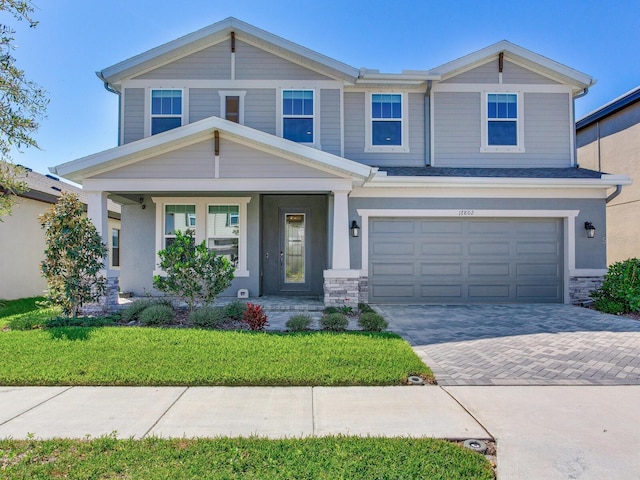 view of front of house featuring a garage, stone siding, decorative driveway, and a front yard