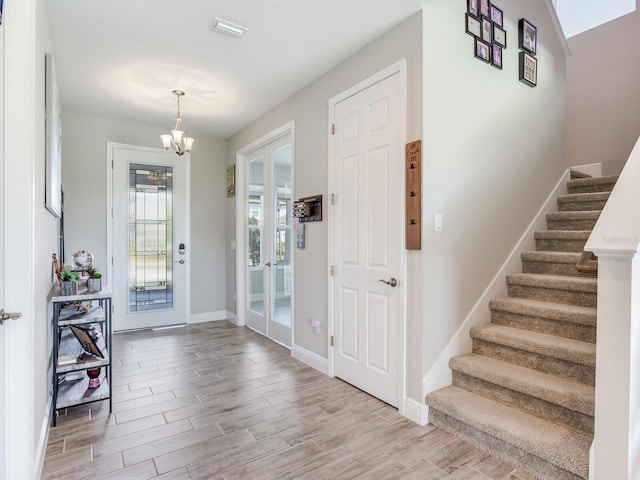 entryway with a chandelier, wood finished floors, visible vents, baseboards, and stairs
