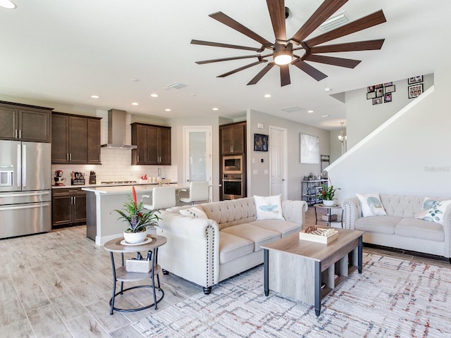 living area with light wood-style floors, ceiling fan with notable chandelier, visible vents, and recessed lighting