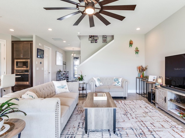 living room featuring baseboards, light wood finished floors, ceiling fan with notable chandelier, and recessed lighting