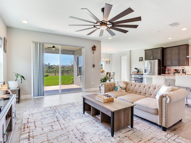 living room featuring light wood-type flooring, ceiling fan with notable chandelier, visible vents, and recessed lighting
