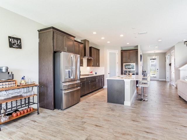 kitchen featuring stainless steel appliances, dark brown cabinets, light countertops, backsplash, and wall chimney exhaust hood
