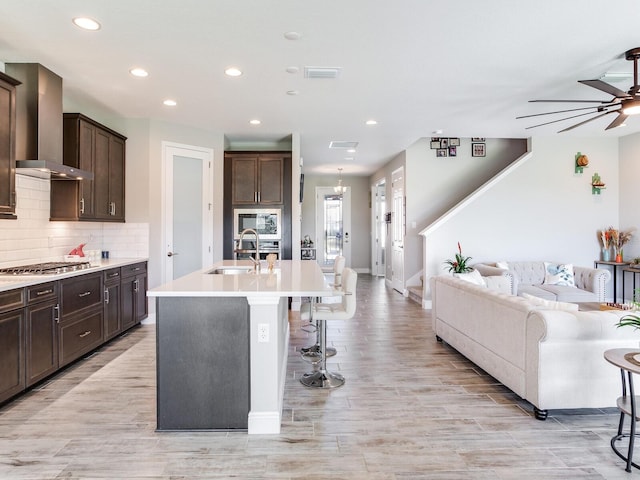 kitchen featuring stainless steel appliances, decorative backsplash, wall chimney range hood, dark brown cabinets, and a kitchen bar