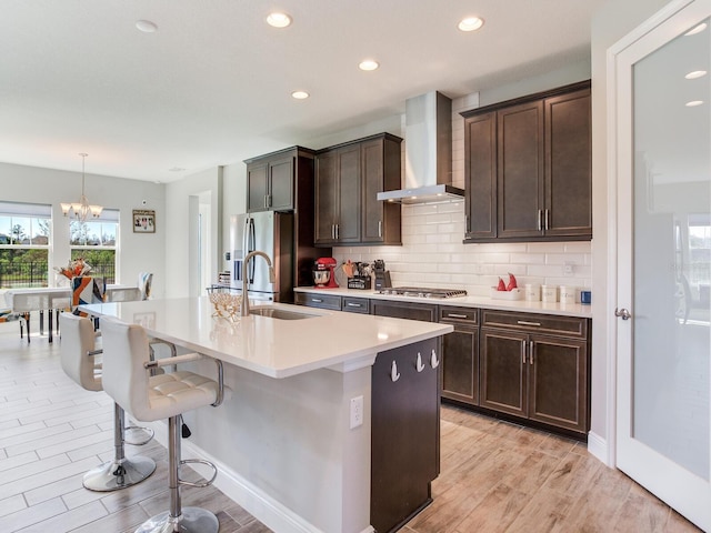 kitchen with an island with sink, a kitchen breakfast bar, stainless steel appliances, wall chimney range hood, and a sink