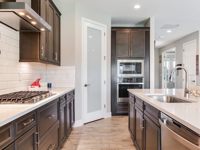 kitchen with tasteful backsplash, visible vents, appliances with stainless steel finishes, range hood, and a sink
