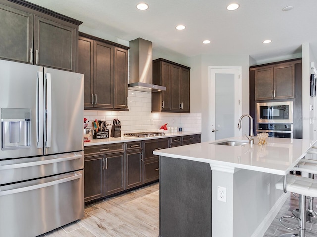 kitchen with a sink, light countertops, appliances with stainless steel finishes, backsplash, and wall chimney exhaust hood