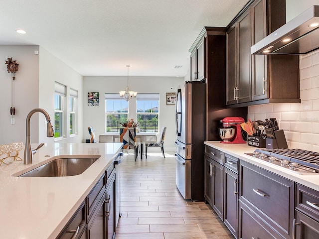kitchen featuring tasteful backsplash, light countertops, appliances with stainless steel finishes, a sink, and wall chimney range hood